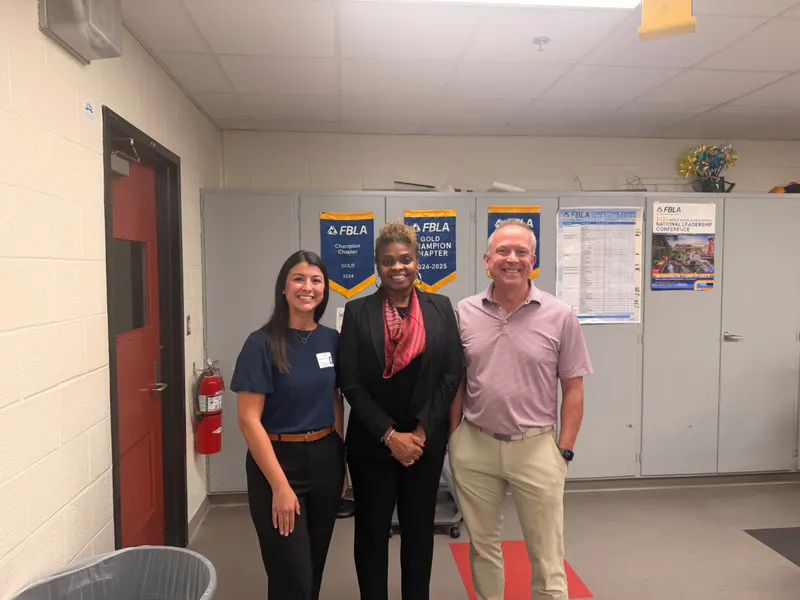 Pamela Coleman with two education partners in front of FBLA achievement banners.